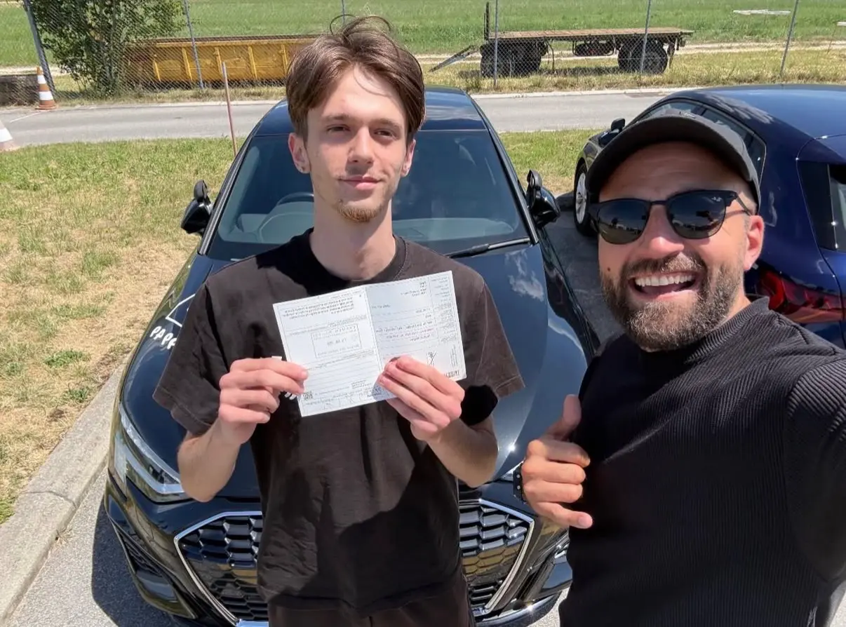 Mergim and his student in a black T-shirt showing their newly earned driving licence.
